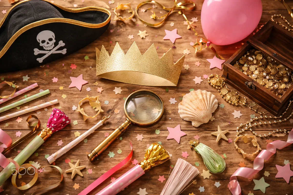 Un plateau en bois sur lequel sont posés un chapeau de pirate en papier, une couronne, une loupe, un coquillage, des étoiles en papier et un ballon
